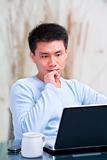 Young Chinese man thinking in front of his laptop
