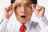 Asian businessman surprised holding glasses to camera
