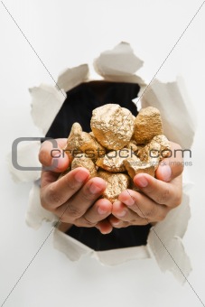 Hand breakthrough wall holding lumps of golden nuggets