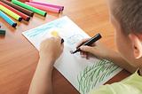 child draws green grass and sun on paper