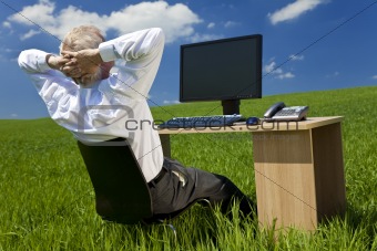Businessman Relaxing at Desk With Computer In A Green Field