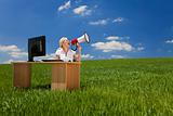 Woman At Desk With Computer Using Megaphone In Green Field