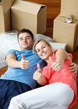 Happy couple on floor after moving with thumbs up