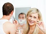 Smiling woman holding pills and man shaving