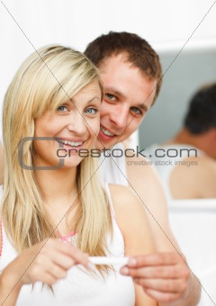 Happy couple looking at a pregnancy test smiling at the camera