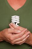 Female Hands Holding Energy Saving Light Bulb Against Green Shirt.