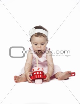 Baby in pink clothes playing with a red toy