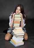 Girl sits on a floor embracing big pile of books