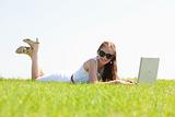 oung female lying on the grass in the park using a laptop