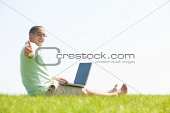 A young men sit on the in the park using a laptop