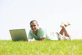 A young men lying on the in the park using a laptop
