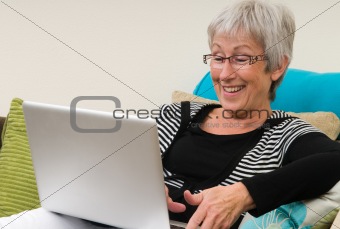 Senior woman working on a laptop, sitting relaxed on the couch.
