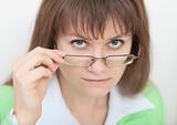 Strict young woman looks at us over eyeglasses