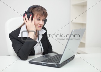 Woman in ear-phones sits with laptop at table at office