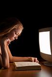 girl reading a book (textbook) in the light of a working compute