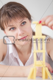 Young girl concentrated builds on table tower of dominoes