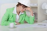 Tired woman - engineer in helmet sits at table in office