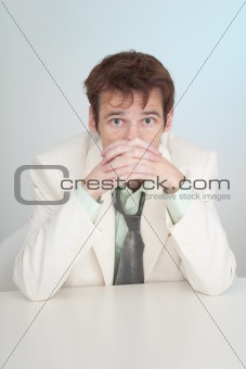 Young sorrowful person in white suit sits at table