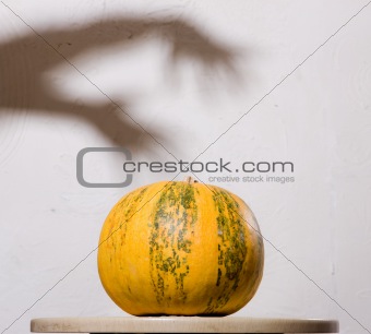 Yellow pumpkin no table with hands shadow on wall