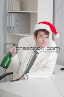 Young man in Christmas cap sits with bottle at table