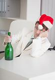 Young businessman in Christmas cap sits with bottle at table