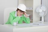Sad woman engineer with helmet on head sits at table on workplac