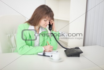 Secretary speaks on the phone doing records in notebook