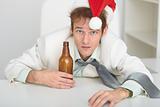 Young man in Christmas hat at office with a beer bottle