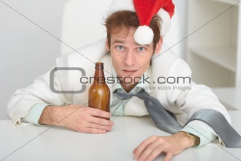 Young man in Christmas hat at office with a beer bottle