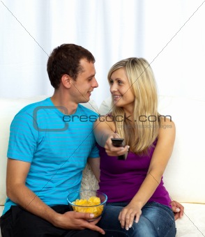 Couple watching television on sofa and eating crisps