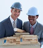 Smiling engineers with hard hats holding a model house