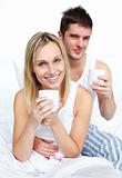 Couple drinking coffee in bed and smiling at the camera