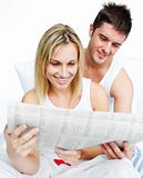 Young couple reading newspaper in bed