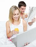 Couple reading a newspaper and using a laptop in bed