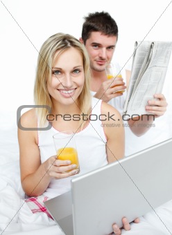 Couple drinking orange juice and reading news in bed