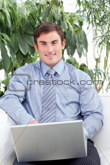 Businessman using a laptop on couch and smiling at the camera