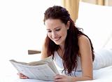 Brunette woman in bed reading a newspaper