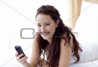 Smiling woman sending a text in bed