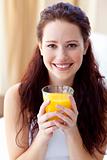 Smiling woman drinking orange juice in bedroom