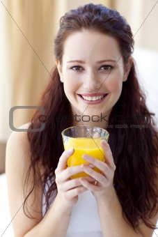 Smiling woman drinking orange juice in bedroom