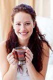 Smiling woman drinking a cup of tea in bedroom