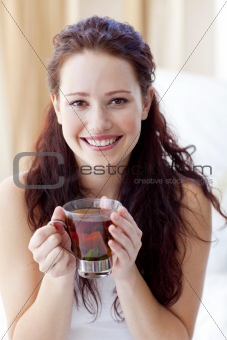 Smiling woman drinking a cup of tea in bedroom