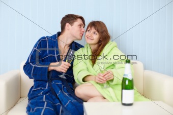 Young pair at home on divan with sparkling wine