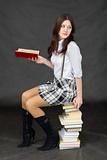 Schoolgirl sits on big pile of books against dark background