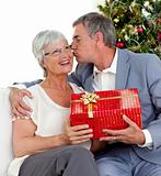 Senior man giving a kiss and a Christmas present to his wife