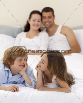 Brother and sister looking at each other in bed with her parents