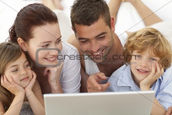Portrait of family in bed using a laptop
