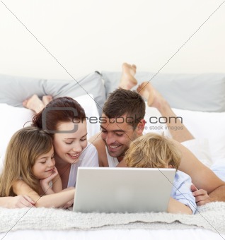 Parents and children in bed playing with a laptop