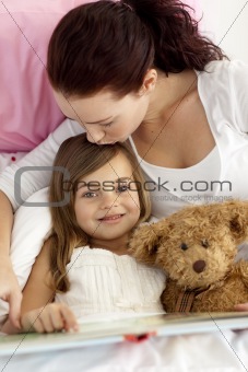 Mother kissing her daughter reading in bed