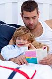 Little son reading with his father in bed